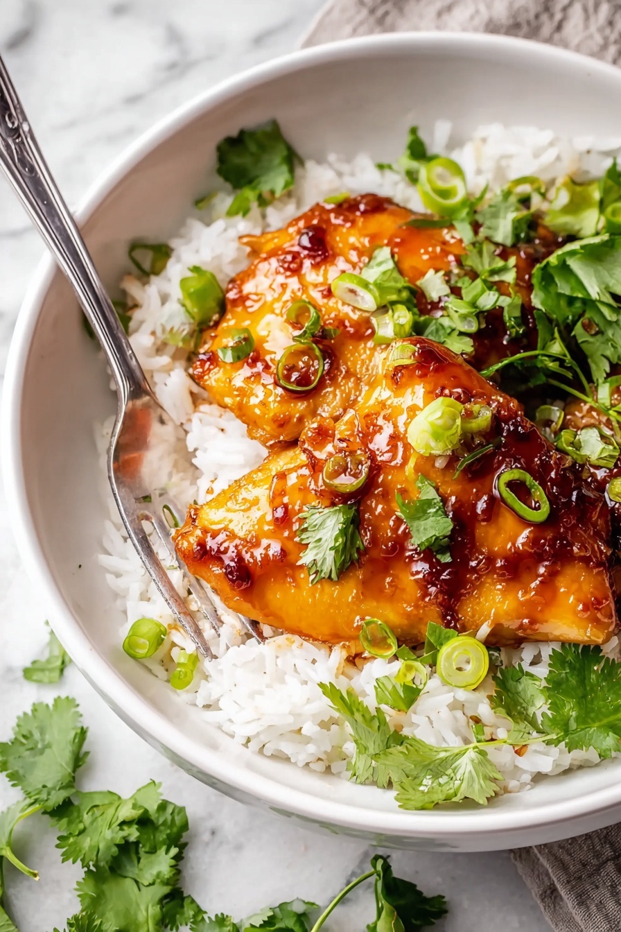 A white bowl filled with a base layer of fluffy white rice, topped with two pieces of golden brown glazed chicken with a shiny, sticky sauce. The chicken is garnished with bright green sliced scallions and fresh cilantro leaves scattered over both the chicken and rice. A silver fork rests inside the bowl on the left side. The bowl sits on a white marbled surface with a bit of greenery visible around. photo taken with an iphone --ar 2:3 --v 7