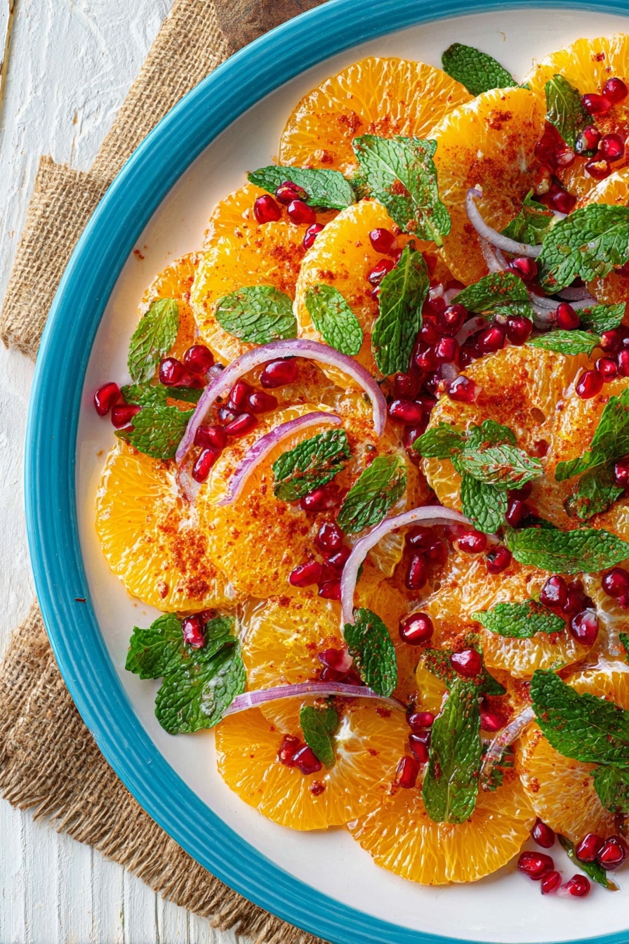 The dish shows a white plate filled with three visible layers of thin, round orange slices arranged neatly in a slightly overlapping pattern covering the plate. On top of the orange slices are thin, curved slices of red onion scattered in between. Bright green mint leaves are spread over the salad, mixed with shiny red pomegranate seeds that add a jewel-like texture. A light dusting of reddish-orange spice powder is sprinkled evenly over the oranges and onions. The plate is set on a white marbled surface with a faint piece of burlap fabric and wooden rustic table visible in the background. photo taken with an iphone --ar 2:3 --v 7
