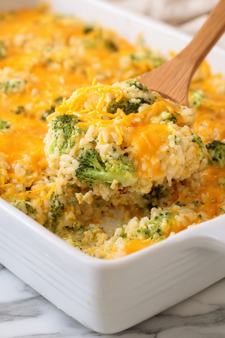 The image shows a white rectangular baking dish filled with a baked broccoli and cheese casserole. The casserole has a base layer made of fluffy, beige rice mixed with green broccoli pieces evenly spread throughout. On top of this is a bright layer of melted orange cheddar cheese, giving a slightly stringy texture. A wooden spoon is scooping a portion from the dish, highlighting the soft, moist interior with visible broccoli chunks and shredded cheese. The dish is placed on a white marbled surface with soft, natural light enhancing the colors. Photo taken with an iphone --ar 2:3 --v 7