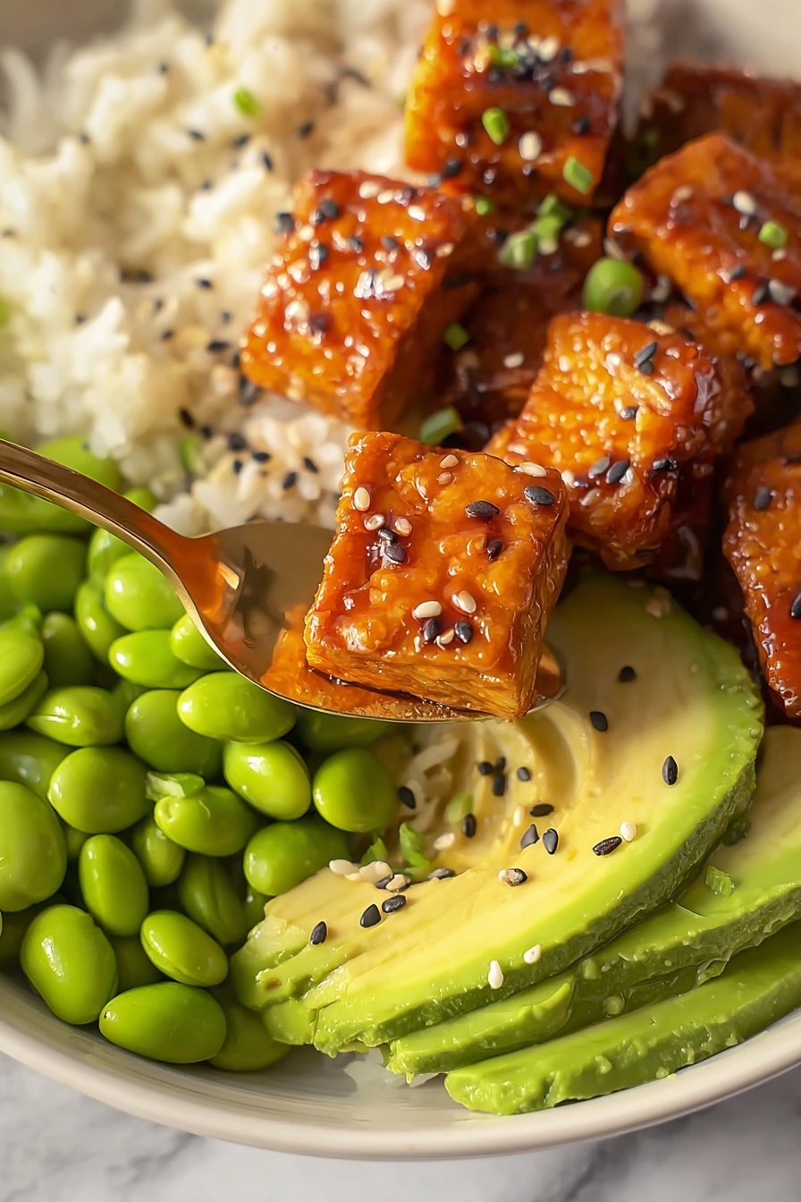 This dish is shown in a close-up view with three main layers visible on a white bowl over a white marbled surface. The bottom layer is white rice with a fluffy texture, taking up the background area. On one side, there is a layer of bright green edamame beans, smooth and shiny. Next to it, there is sliced avocado arranged in thin, curved slices with a creamy light green color. On top, there are several pieces of glazed tempeh with a rich orange-brown color, shiny and sticky, sprinkled with black and white sesame seeds. A gold spoon holds a couple of tempeh pieces up front, showing more detail. The photo is taken with an iphone --ar 2:3 --v 7