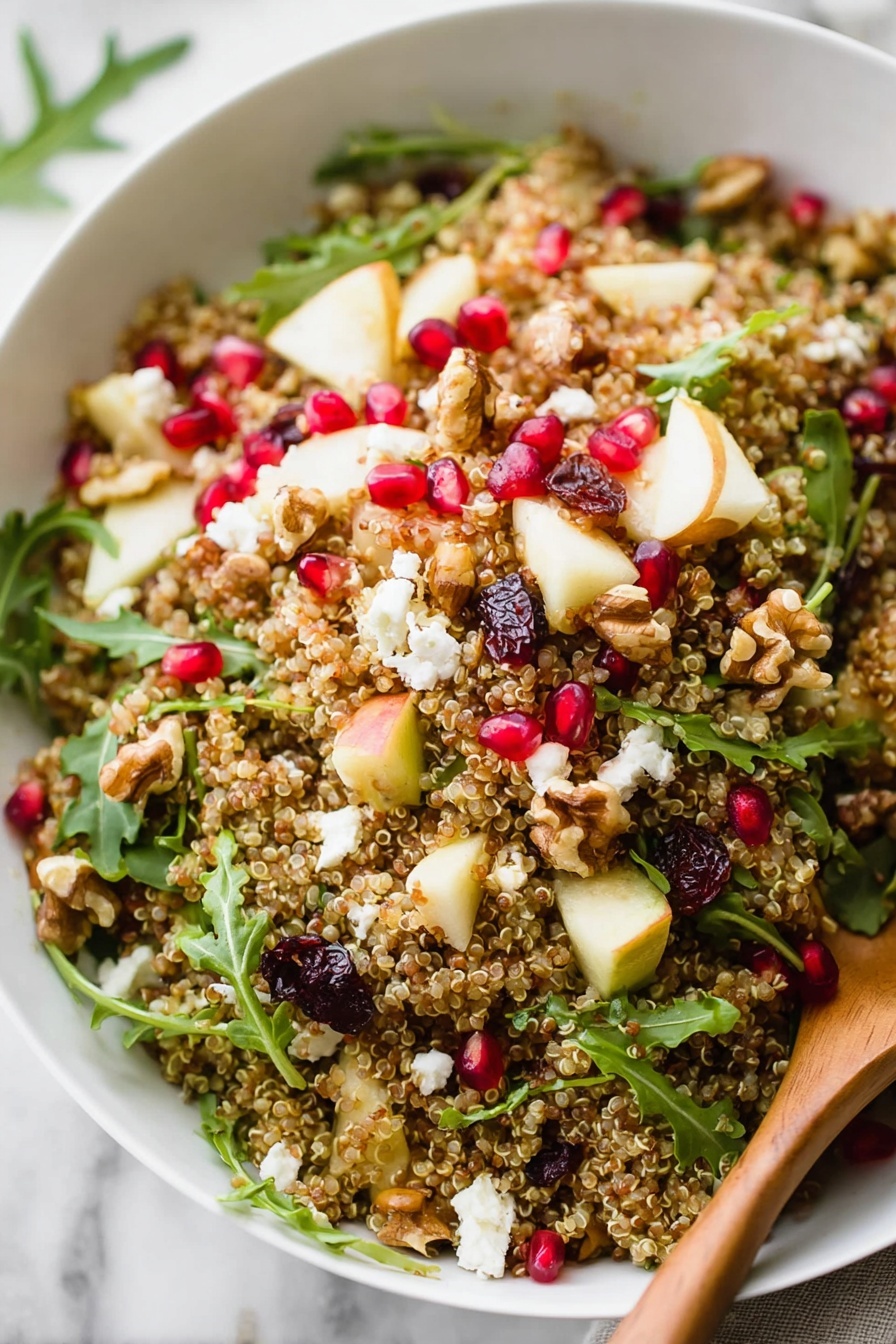 A white bowl is filled with a colorful quinoa salad on a white marbled surface. The salad has a grainy layer of light brown quinoa, topped with small pieces of white cheese, bright red pomegranate seeds, chunks of pale yellow apple, green arugula leaves, and dark red dried cranberries. A few pieces of walnuts add texture throughout. A wooden spoon rests on the right side of the bowl, partially in the salad. Around the bowl, loose quinoa grains, some arugula leaves, and pomegranate seeds are scattered, with a halved pomegranate showing deep red seeds in the upper part of the image. photo taken with an iphone --ar 2:3 --v 7