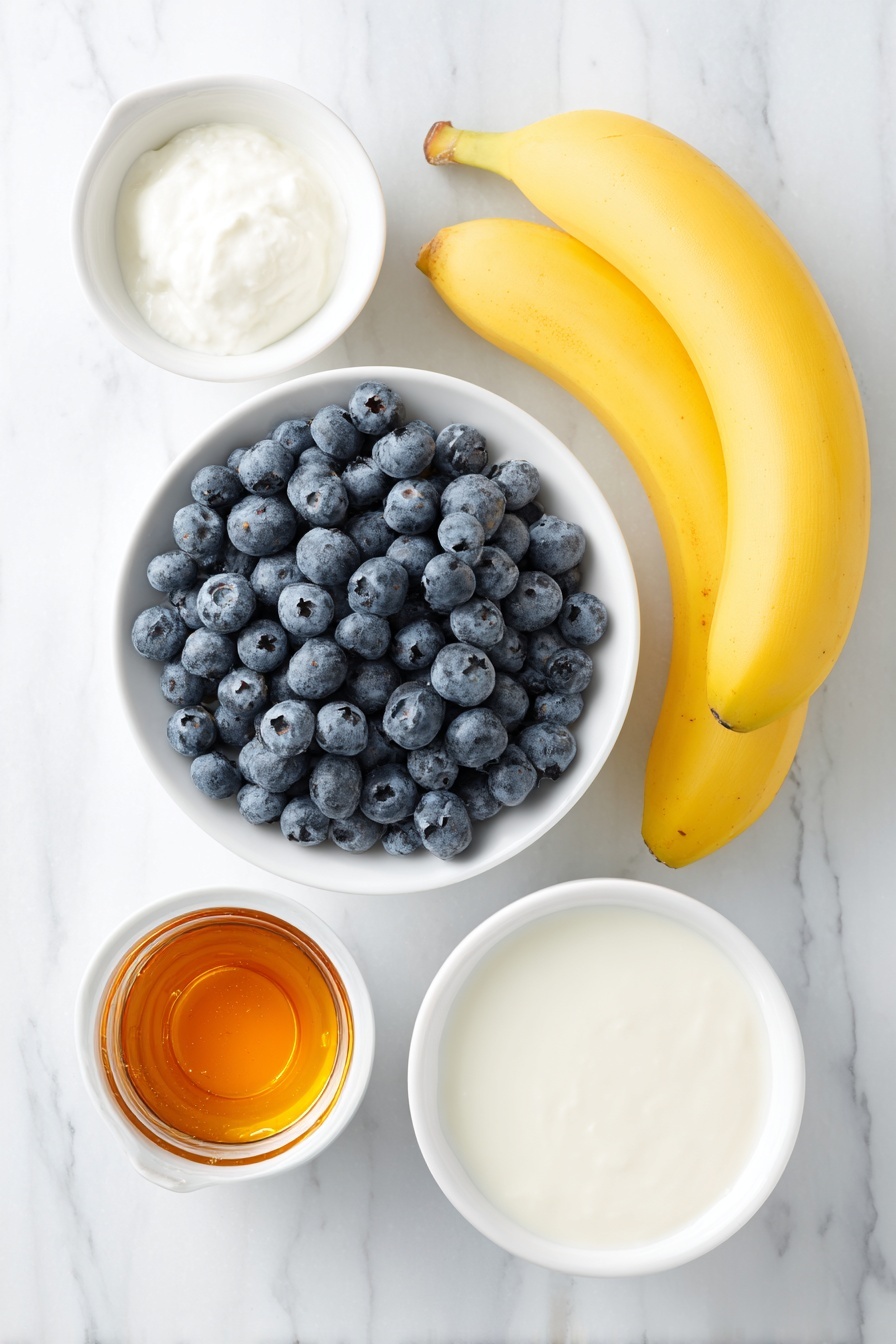 Flat lay of fresh blueberries scattered beside a whole ripe banana with bright yellow skin, a small white ceramic bowl of smooth almond milk, a small white ceramic bowl of light creamy coconut milk, and a small white ceramic bowl filled with amber maple syrup, all arranged with perfect symmetry on a clean white marble surface, soft natural light, photo taken with an iPhone, professional food photography style, fresh ingredients, white ceramic bowls, no bottles, no duplicates, no utensils, no packaging --ar 2:3 --v 7 --p m7354615311229779997