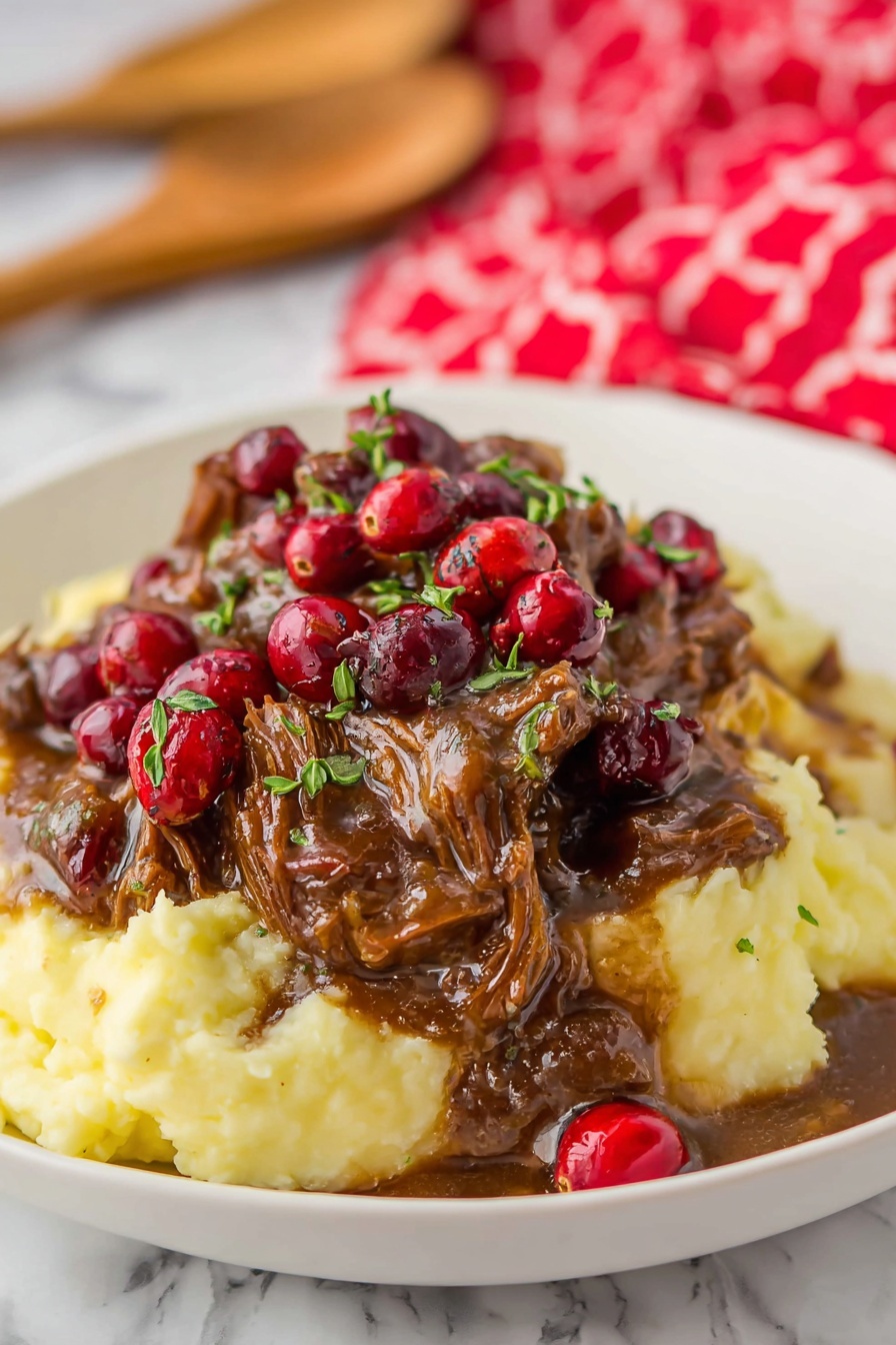 A white round plate holds a dish with three main parts: a bottom layer of creamy light beige mashed potatoes with a smooth and fluffy texture, topped in the middle by a layer of brown shredded meat covered in thick dark brown gravy and bright red fresh cranberries, some green herbs sprinkled on top; to the right side of the plate, a neat row of bright green cooked asparagus spears with slight grill marks. Behind the plate, there is a small white bowl full of red cranberries, placed on a red plaid cloth on a wooden cutting board. The background is a white marbled surface. Photo taken with an iphone --ar 2:3 --v 7