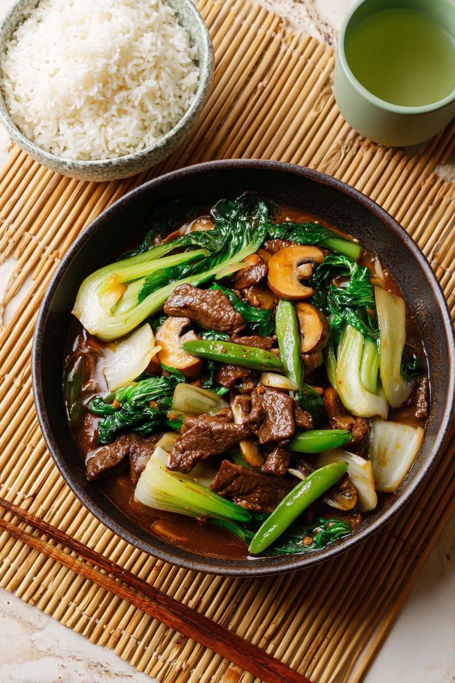 The image shows a dark brown bowl filled with stir-fried beef and vegetables. The dish has layers of glossy dark brown beef pieces mixed with bright green snap peas and dark green leafy greens. There are also light yellowish-white slices of bok choy and small brown mushrooms scattered throughout. The ingredients are coated in a shiny brown sauce. The bowl sits on a light brown woven mat with a pair of wooden chopsticks resting next to it. In the background, there is a white bowl with blue patterns holding white rice and a small green cup with tea, all placed on a white marbled surface. Photo taken with an iphone --ar 2:3 --v 7