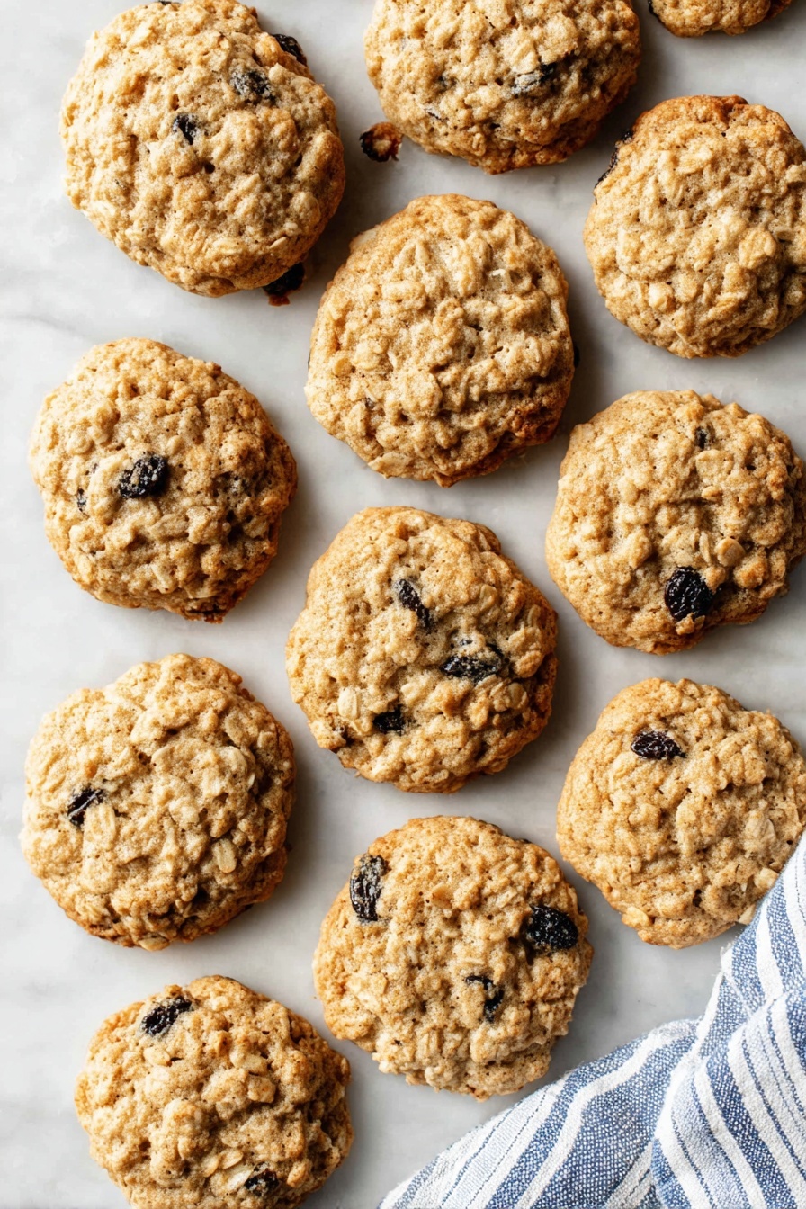 A group of round oatmeal raisin cookies with a light golden brown color and a rough texture from oats and raisins scattered across a white marbled surface, some cookies slightly overlapping one another, with a blue and white striped cloth lying on the bottom right side; the cookies have visible dark raisin pieces and a slightly cracked top, showing a homemade appearance. photo taken with an iphone --ar 2:3 --v 7