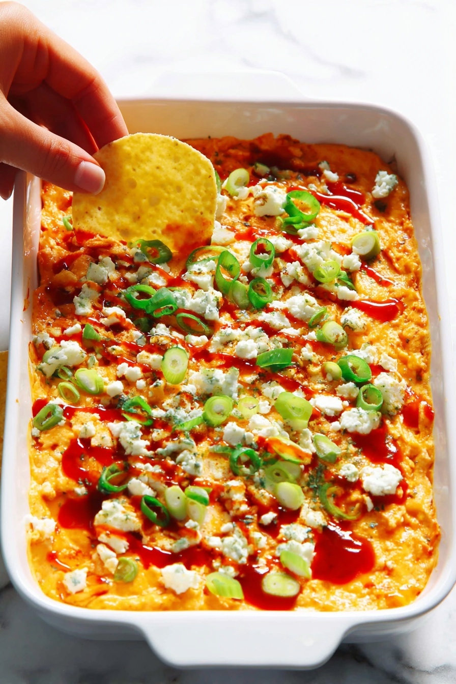 The image shows a clear glass bowl filled with a creamy, chunky orange mixture that looks thick and textured. There are small bits of green herbs scattered throughout the mixture, which has a soft and slightly uneven texture. A red and black spatula is partially stuck into the mixture from the left side of the bowl. The bowl is placed on a white marbled surface. photo taken with an iphone --ar 2:3 --v 7
