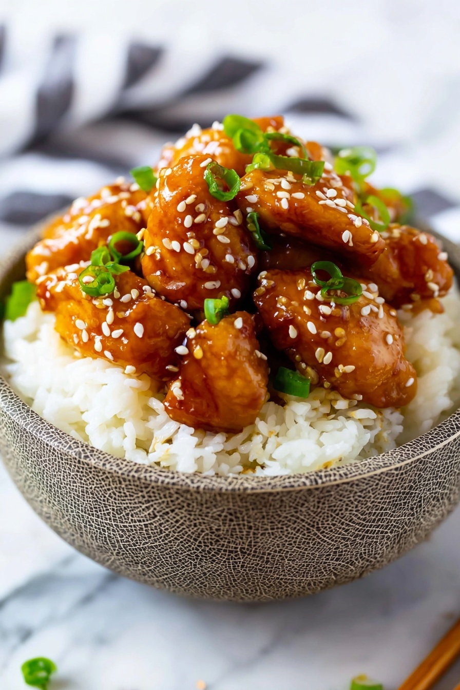 A bowl with a cracked pattern holds a bed of white, fluffy rice at the bottom, topped with several glossy, brown glazed chicken pieces arranged in a small mound. The chicken has a shiny, smooth texture, coated evenly with sauce. Scattered over the chicken are small white sesame seeds and bright green chopped scallions, adding color contrast. The bowl sits on a white marbled surface with blurred chopsticks and a striped cloth in the background. photo taken with an iphone --ar 2:3 --v 7